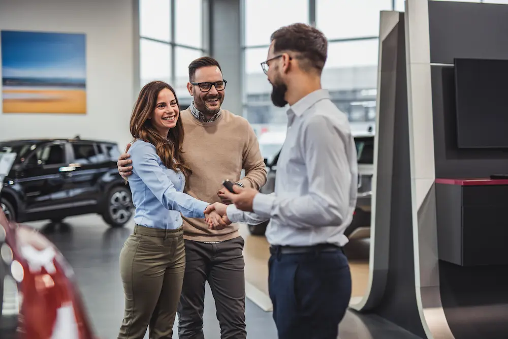 Una pareja feliz recibe las llaves de su coche nuevo de manos del vendedor